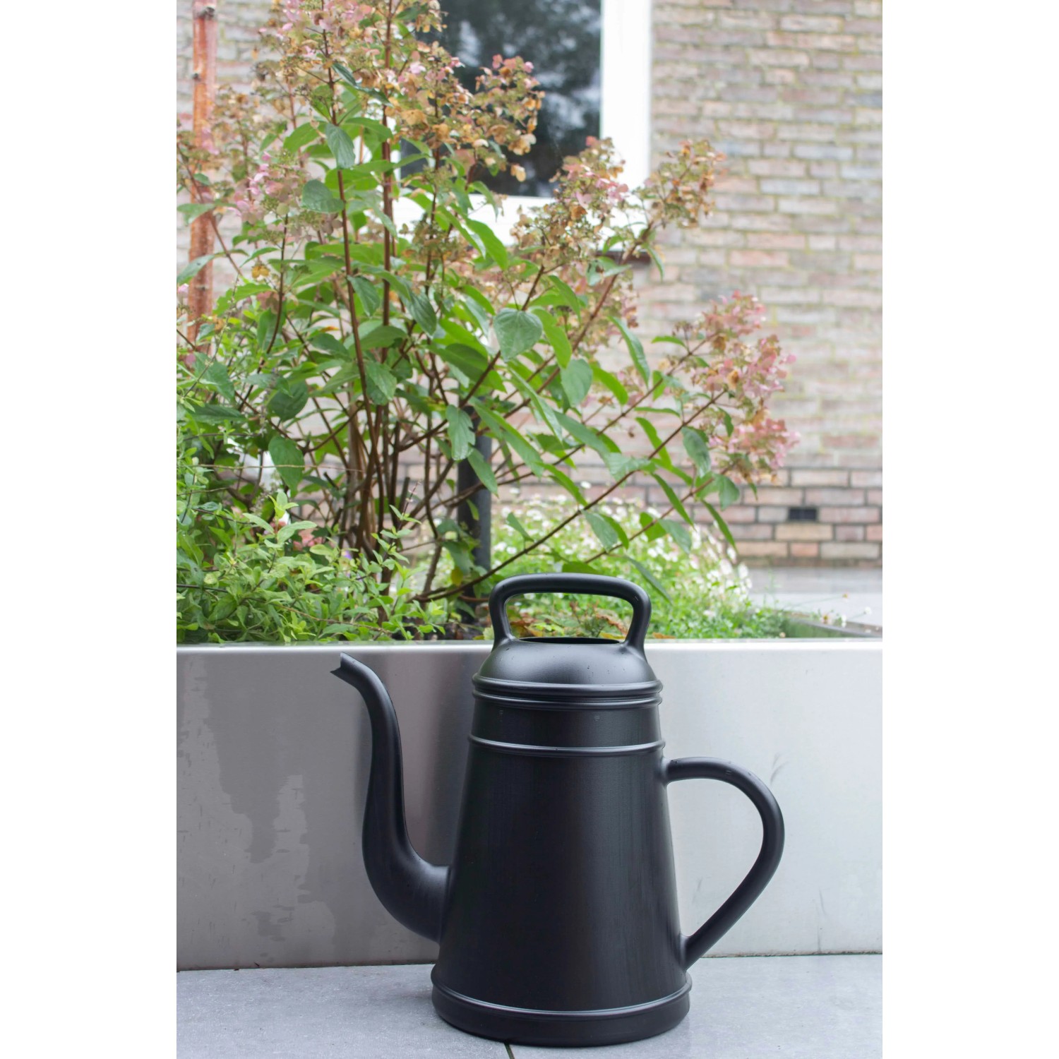 Schwarze Xala Gießkanne (8 l) vor Pflanzenkübel. Design-Gießkanne für Garten und Innenbereich.