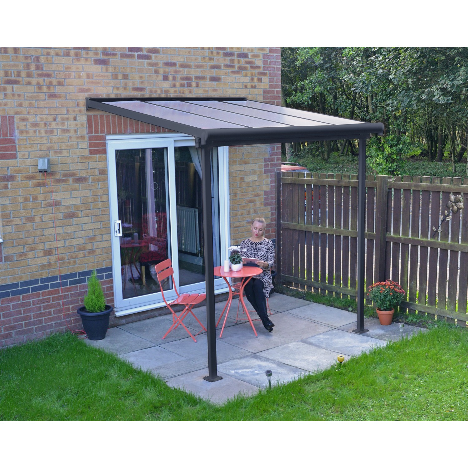 Graues Palram Terrassendach Sierra 230x230 cm mit Frau an Tisch und Stühlen auf Terrasse.