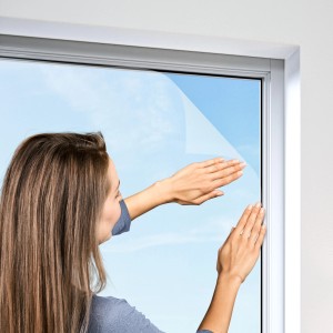 Frau befestigt Windhager Fliegengitter Plus Anthrazit am Fenster. Insektenschutz.