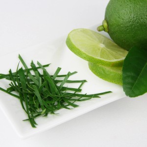 Kaffir-Limette: Ganze Frucht, Limettenscheiben und geschnittene Blätter auf weißem Teller.