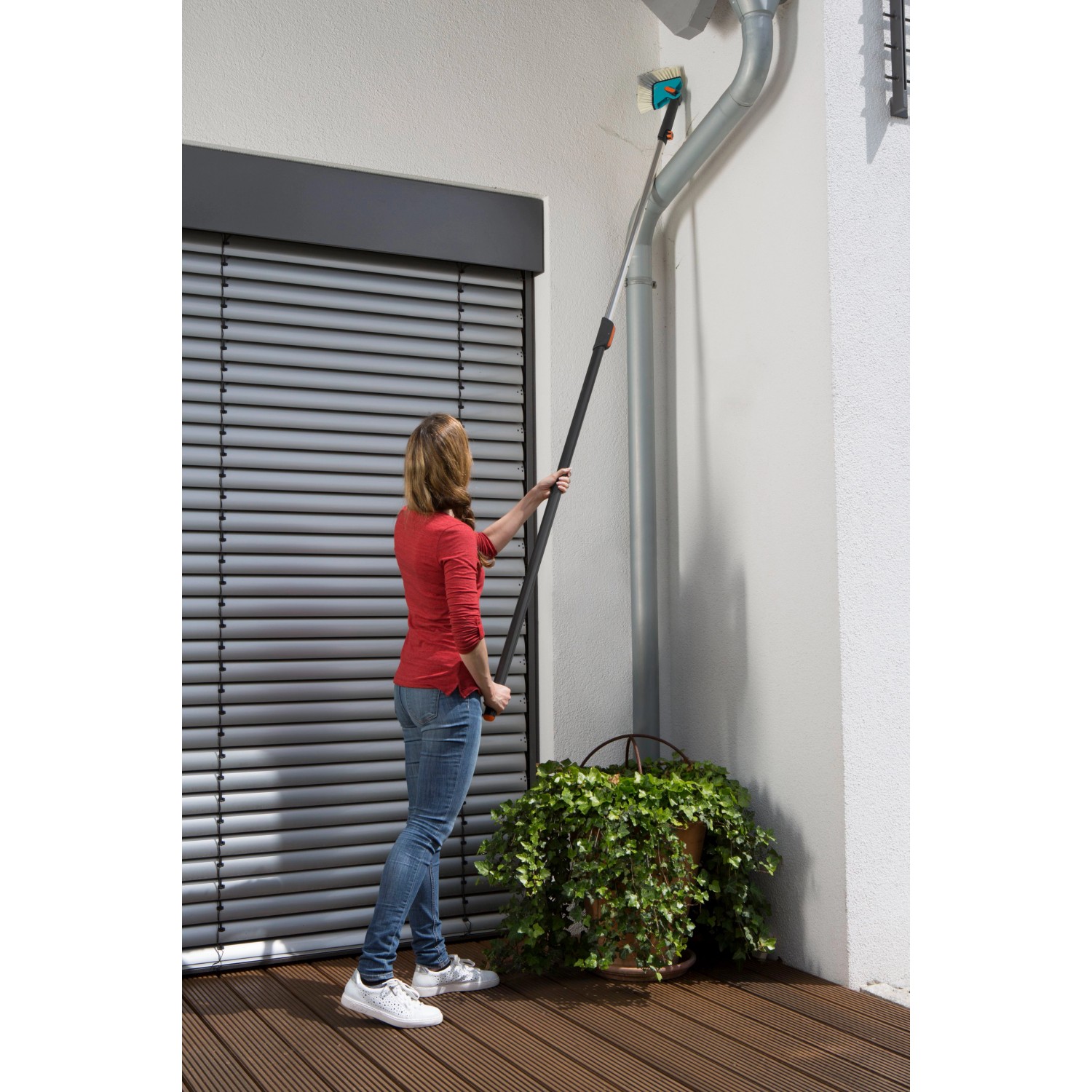 Frau nutzt Gardena combisystem Winkelbesen mit Stiel zur Reinigung einer Dachrinne.