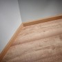 Eckansicht: Holzfarbene Sockelleiste auf Laminatboden, angebracht mit wolfcraft Montage-Set.