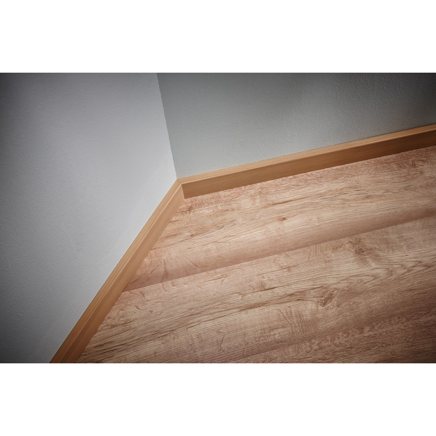 Eckansicht: Holzfarbene Sockelleiste auf Laminatboden, angebracht mit wolfcraft Montage-Set.