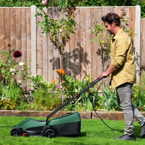 Mann mäht Rasen mit grünem Bosch Easy Rotak 32-235 Elektrorasenmäher im Garten. Kabelgebundenes Gerät mit Fangkorb.