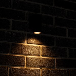 Anthrazitfarbene LED Außenwandleuchte an einer Backsteinwand mit Lichtkegel nach unten.