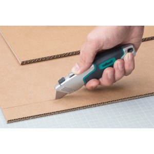 Hand schneidet Pappe mit wolfcraft Profi-Dualklingen-Messer. Trapezklinge sichtbar.