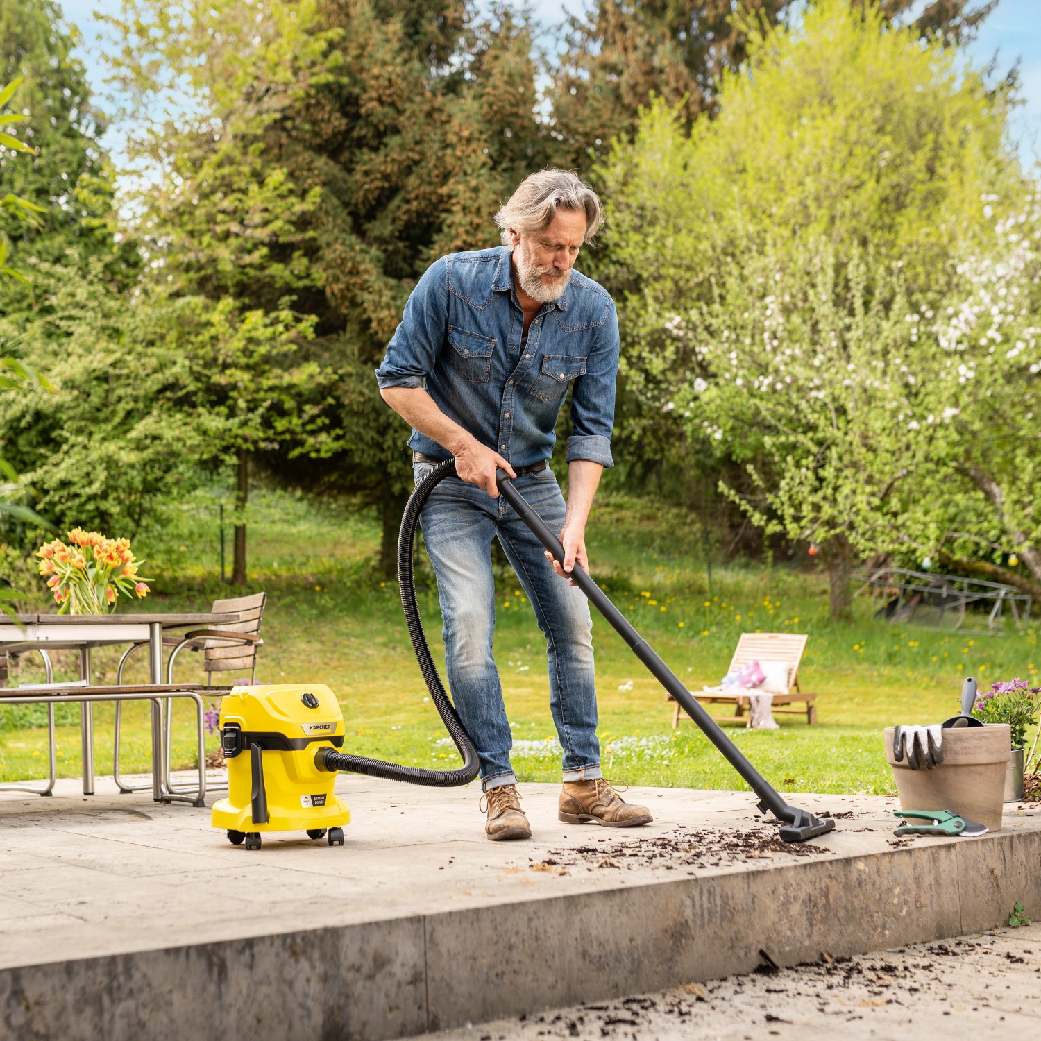 Mann saugt mit gelbem Kärcher Akku Nass-Trockensauger WD 2-18 Schmutz auf Terrasse.