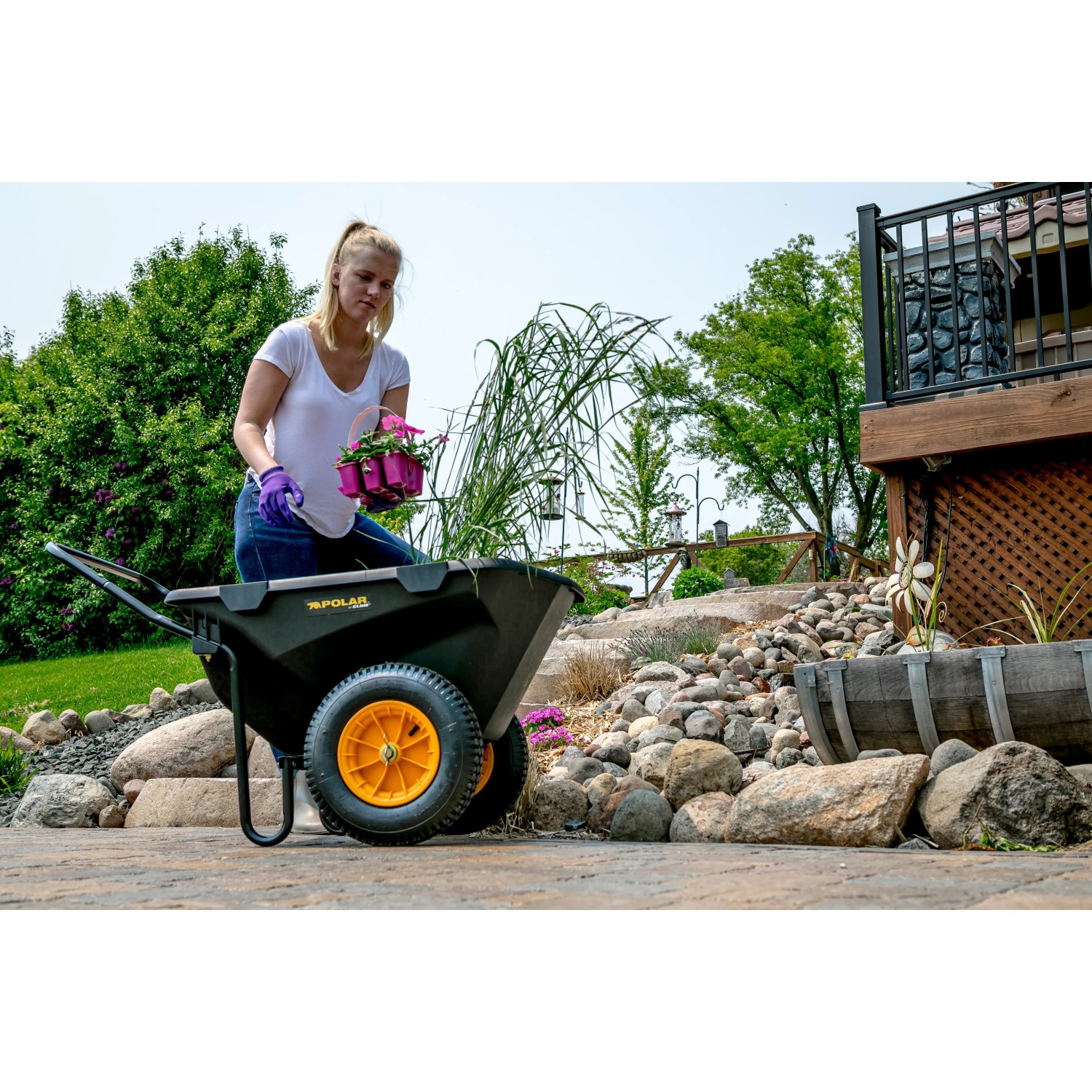 Schwarze Polar Schubkarre Cub Cart (127x71cm) mit Frau und Blumen im Garten.