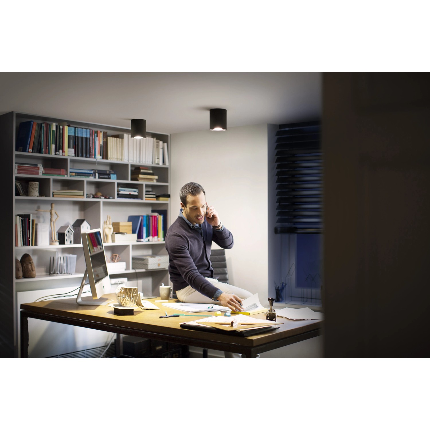 Schwarzer Philips Hue LED-Aufbauspot Pillar White Ambiance im Wohnraum, mit Mann am Schreibtisch.