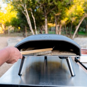 Ooni Pizzaofen-Bürste im Einsatz zum Reinigen eines Pizzaofens. Grillutensil mit Holzgriff.