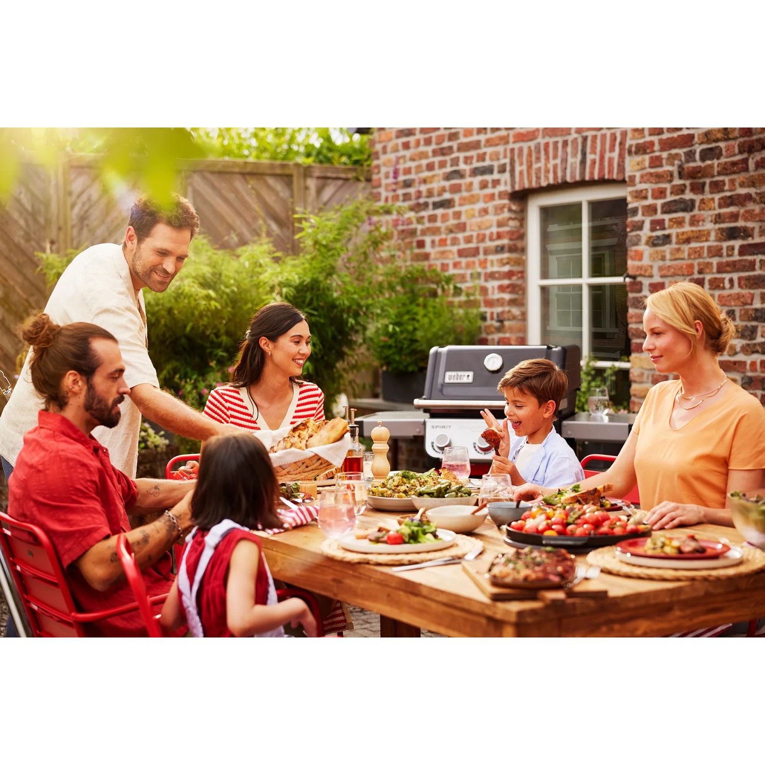 Weber Gasgrill E-210 Spirit (Schwarz) mit Familie beim Grillen im Garten.