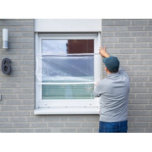 Mann befestigt transparente LUX Fensterschutzfolie am Fensterrahmen.