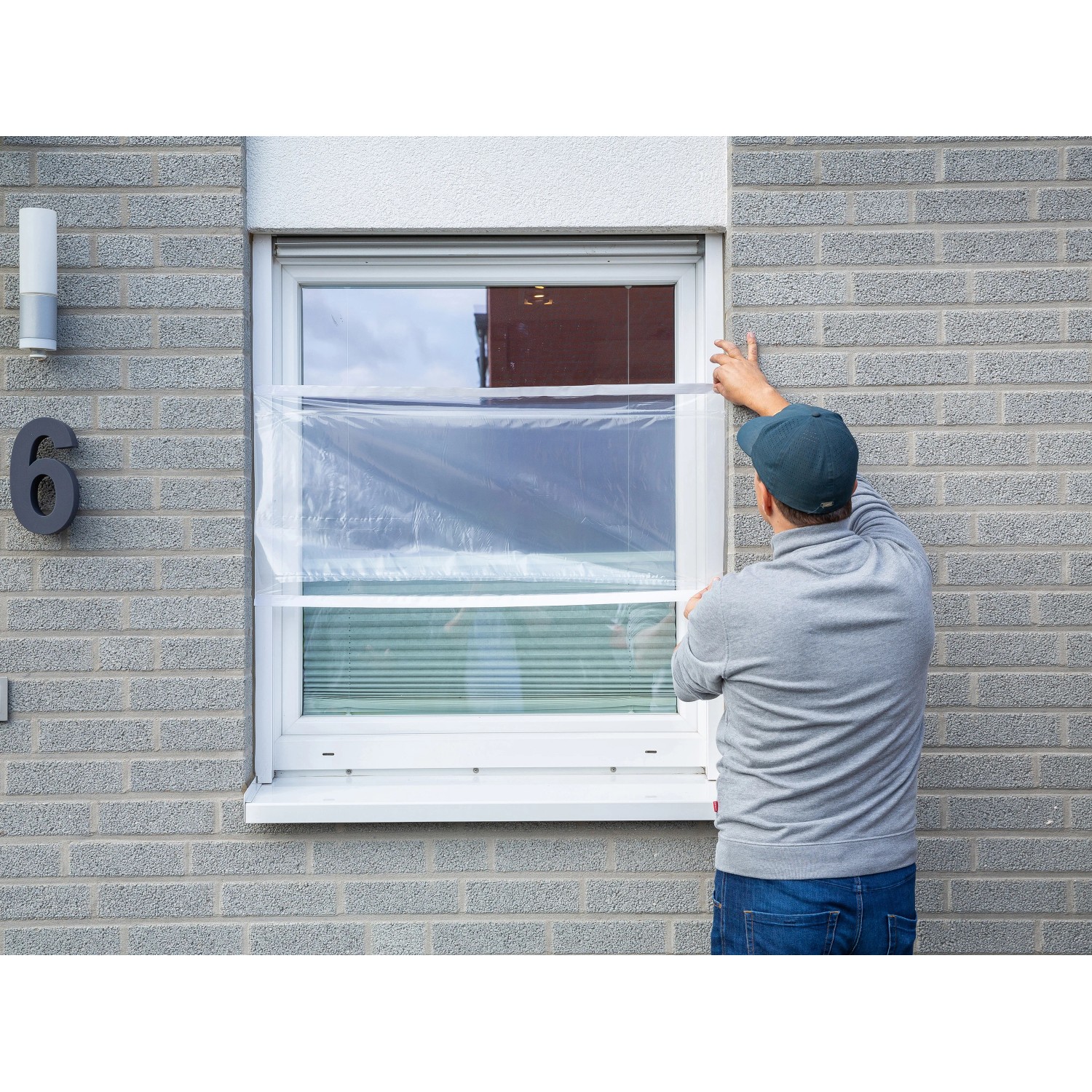 Mann befestigt transparente LUX Fensterschutzfolie am Fensterrahmen.