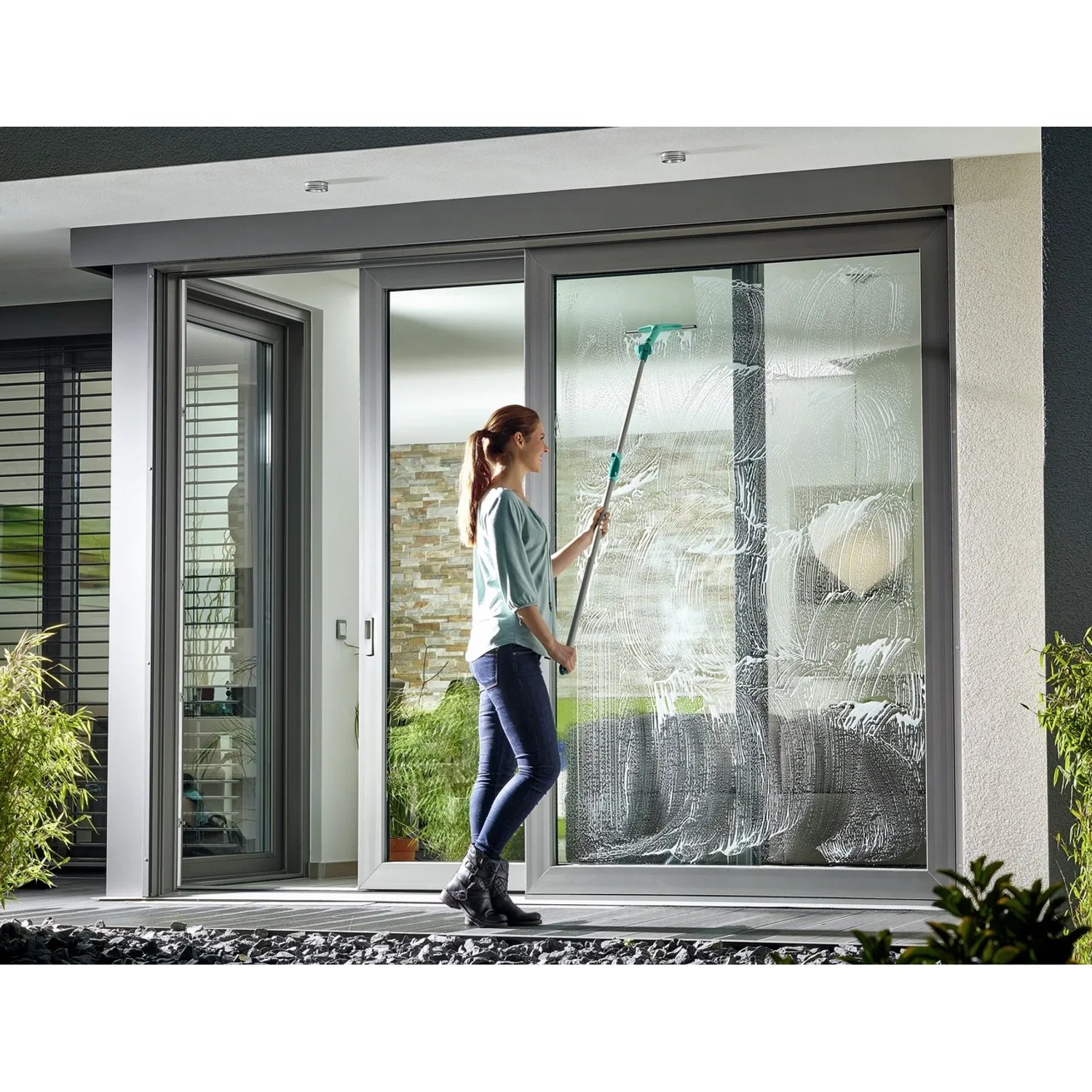 Frau reinigt Fenster mit Leifheit Fensterabzieher Window Slider M. Reinigungsgerät mit Stiel.
