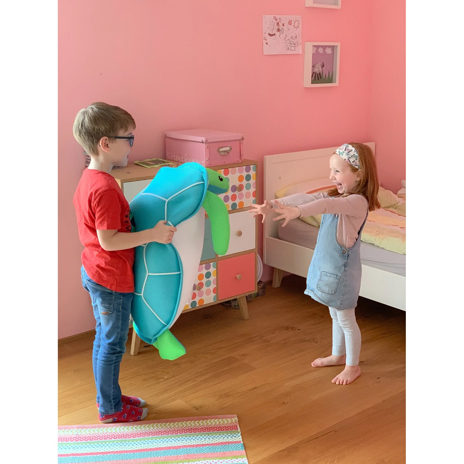 Junge hält blaue Westmann Pool Buddy Schildkröte, Mädchen freut sich im Kinderzimmer.