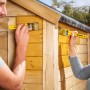 Holzschutzlasur Farblos: Zwei Personen streichen ein Holzhaus mit der Xyladecor Lasur.