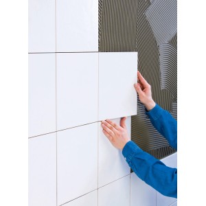 Fliesenleger verarbeitet mit grauem Knauf Superkleber weiße Fliesen an der Wand.