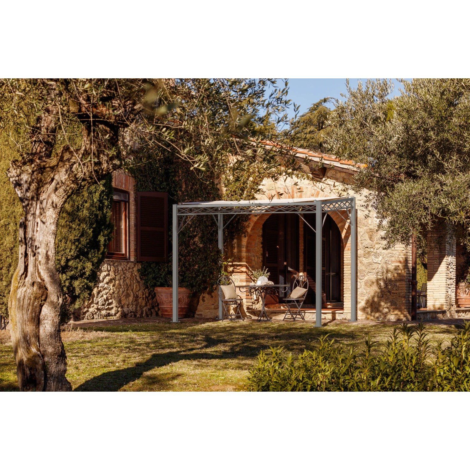Anthrazitfarbene Eleo Pergola Ischia aus Metall, 252,2 x 308 x 204 cm, vor einem Haus mit Tisch und Stühlen.