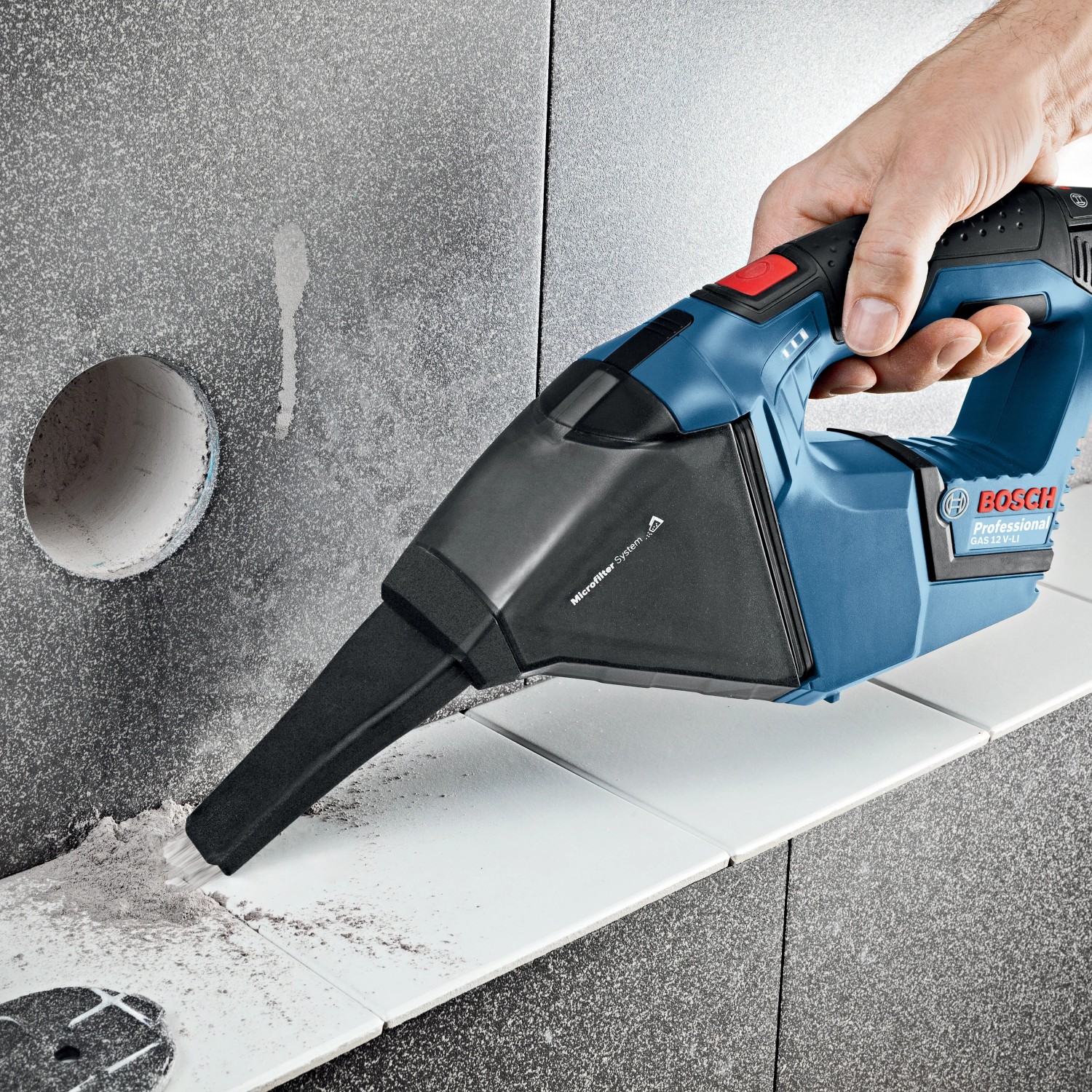 Bosch Akku-Handstaubsauger GAS 12 V-LI in Aktion, blau/schwarz, mit Fugendüse zum Reinigen von Fliesen.
