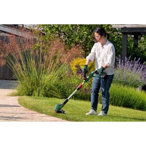 Frau trimmt Rasenkante mit Bosch Akku-Rasentrimmer UniversalGrassCut 18V-26-500 im Garten.