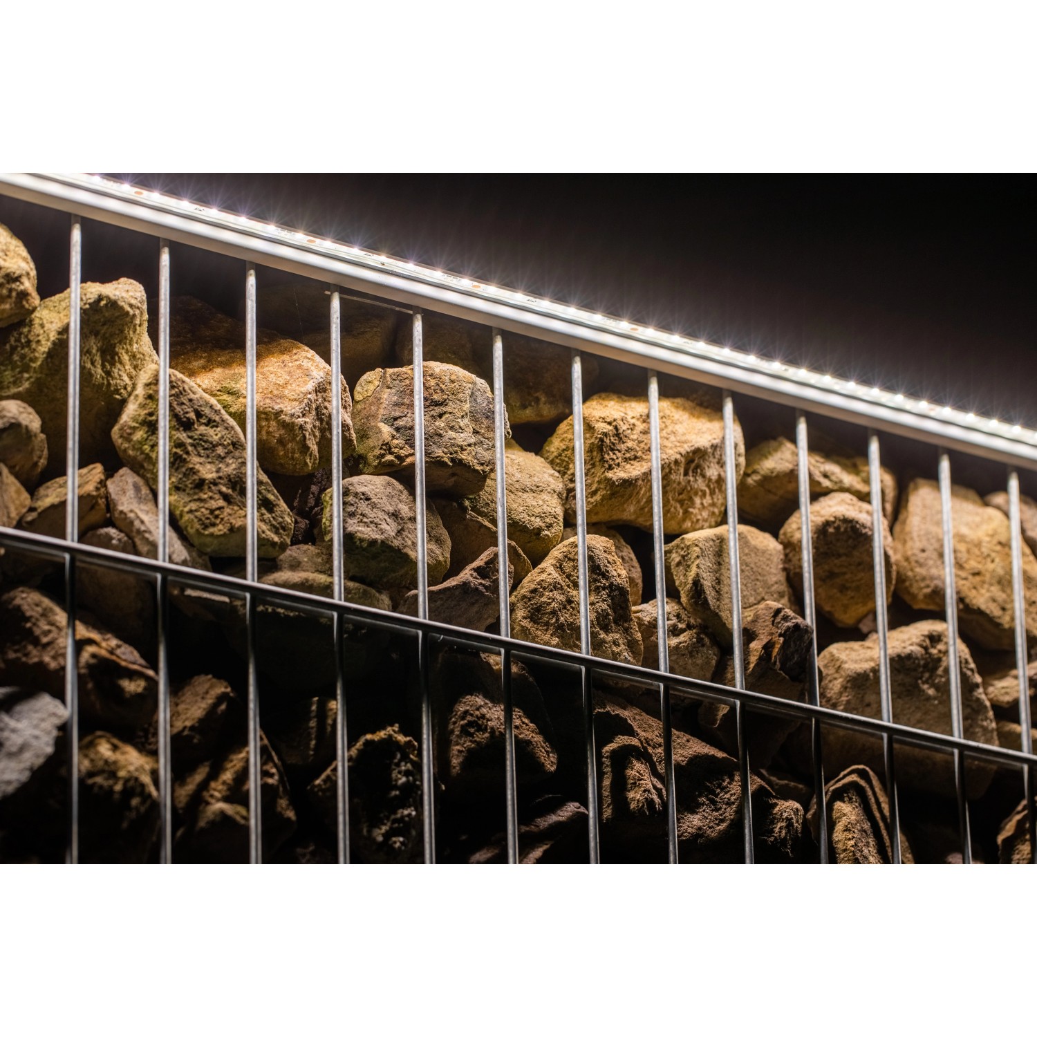 LyghtUp LED-Zaunbeleuchtung Set, anthrazit, mit Steinen in einem Gitterzaun.