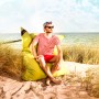 Mann sitzt entspannt auf grünem Sitting Point Sitzsack Big Foot am Strand.