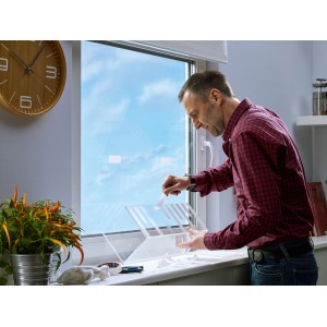 Mann befestigt transparente Platte mit Tesa Montageband an einem Fenster.