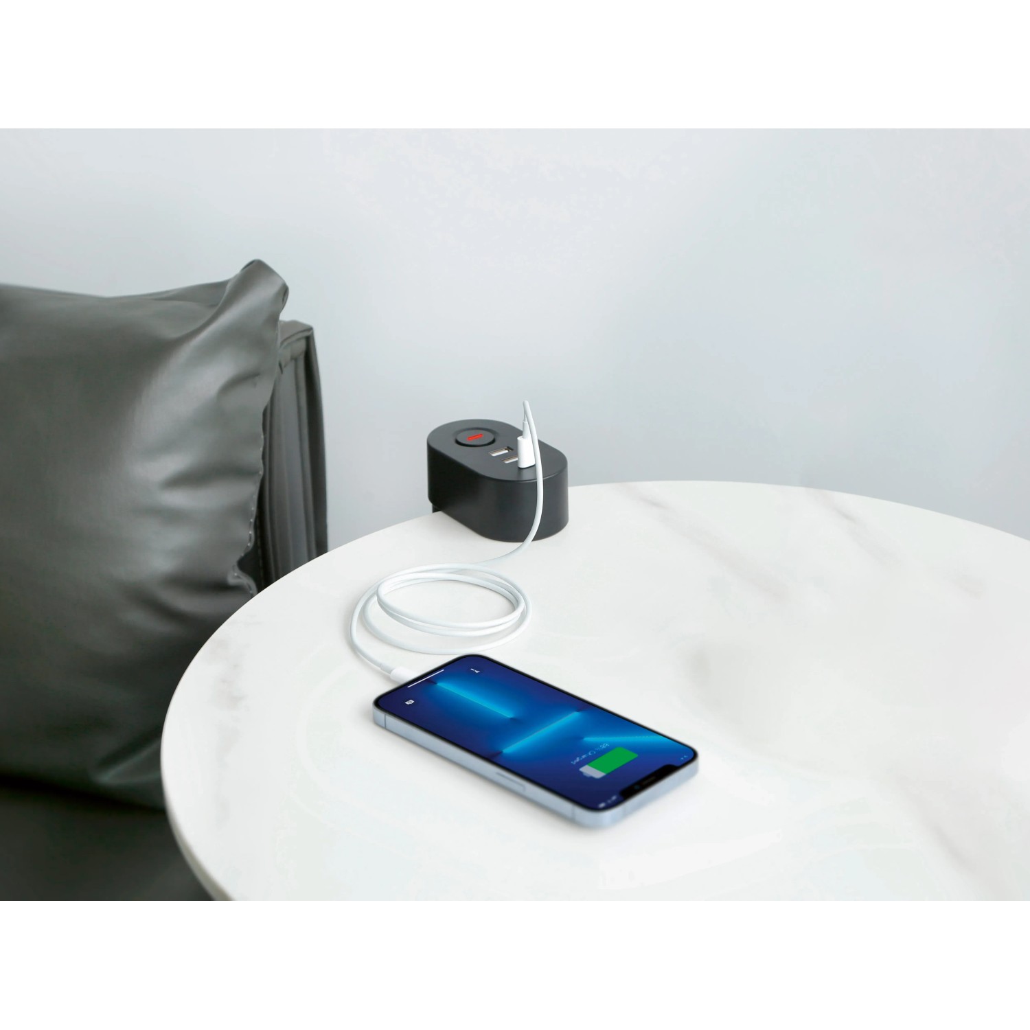 Schwarze 3-fach Steckdosenleiste mit USB-Anschlüssen und Smartphone auf einem Tisch.