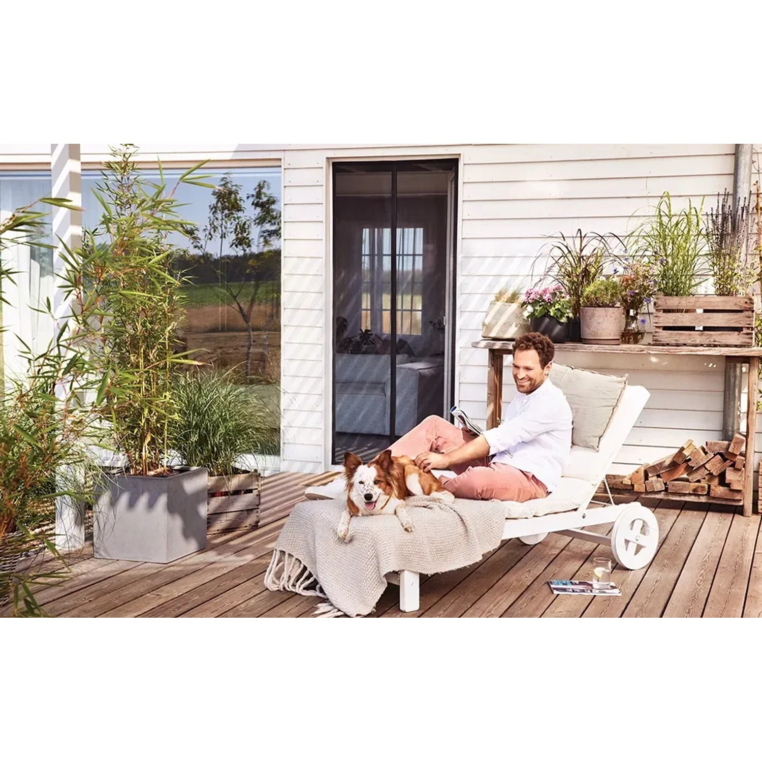 Mann entspannt mit Hund auf Terrasse, geschützt durch tesa Magnetvorhang Anthrazit.