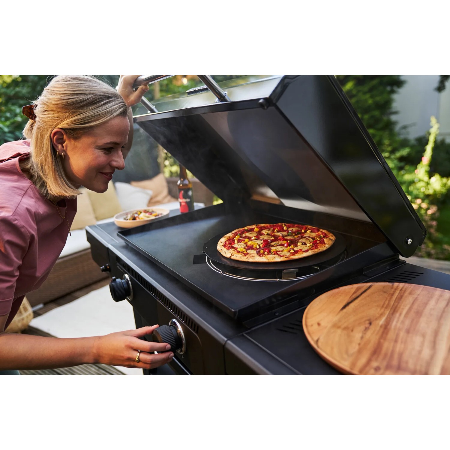 Frau backt Pizza auf Char-Broil Versa-Tile Griddle Gasgrill mit Pizza-Aufsatz.