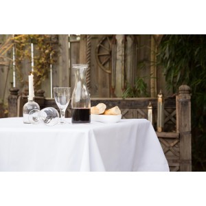 Gedeckter Tisch mit weißer Floracord Tischdecke (110x140 cm), Gläsern, Karaffe und Brot.