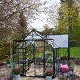 Schwarzes Halls Gewächshaus Garden Room 12,9 m² im Garten mit Pflanzen und Sitzbereich.