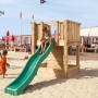 Hy-Land Spielgerät P1 mit Rutsche aus Douglasie auf einem Sandstrand mit spielenden Kindern.