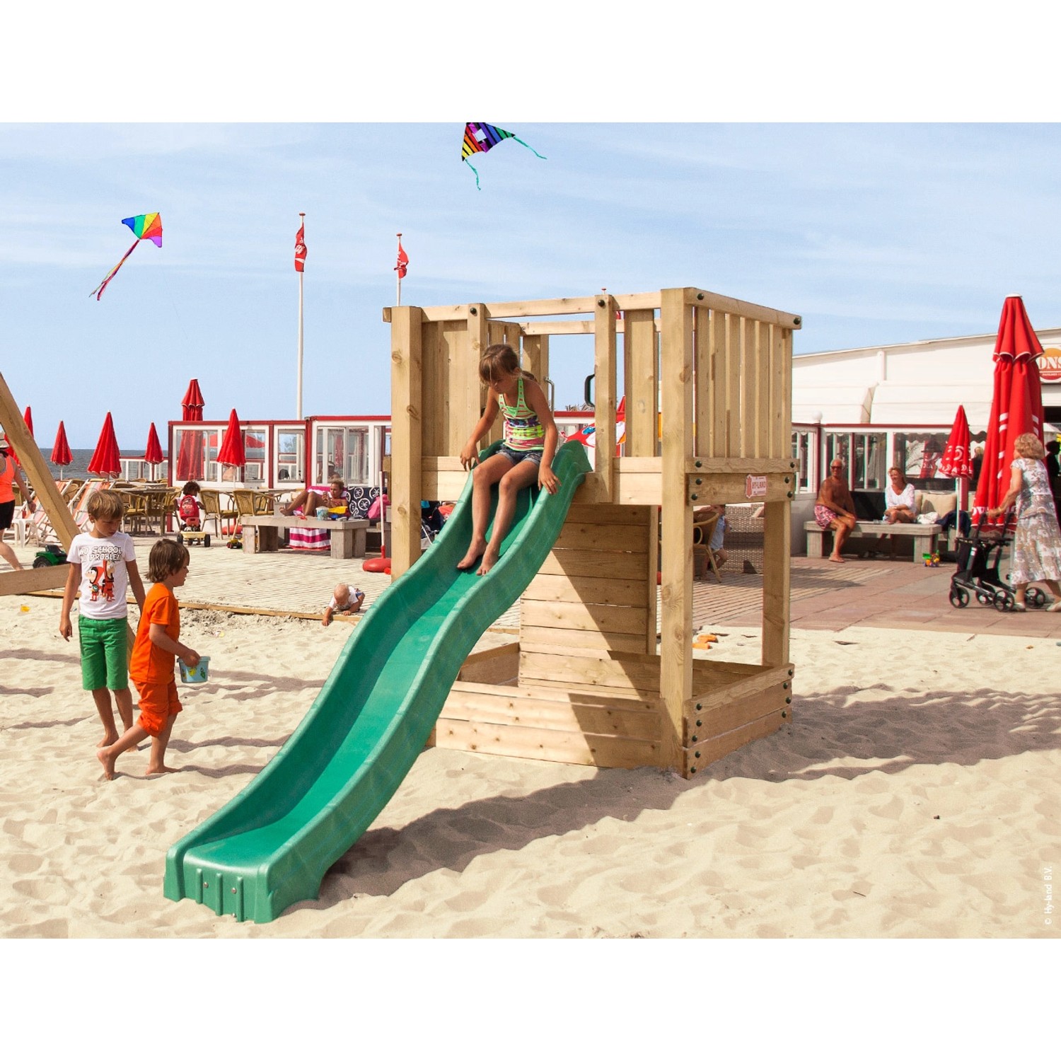 Hy-Land Spielgerät P1 mit Rutsche aus Douglasie auf einem Sandstrand mit spielenden Kindern.