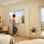 Frau öffnet Fenster mit tesa Insect Stop Fliegengitter Premium in Weiß. Effektiver Insektenschutz.