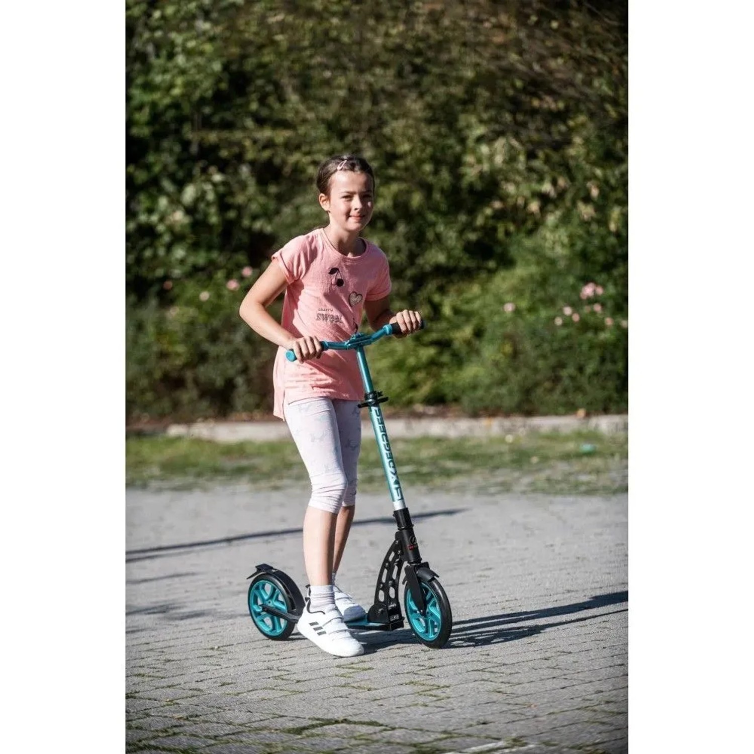 Mädchen fährt türkisen Six Degrees Aluminium Scooter mit Klappmechanismus auf gepflastertem Weg. Höhenverstellbarer Sportroller.