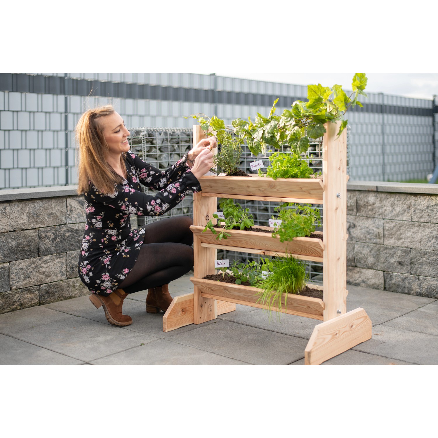 Westmann Kräuterregal Premium L mit Rankgitter bepflanzt mit Kräutern und einer Frau die diese pflegt.