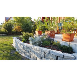 Gartenmauer aus grauen Granitblöcken (40x20x10 cm) von Häusler Naturstein, bepflanzt mit Blumen und Pflanzen.