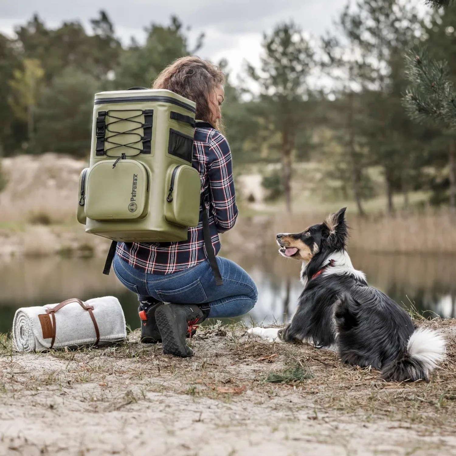 Frau mit grauem Petromax Kühlrucksack 7l und Hund am See. Ideal für Outdoor-Aktivitäten.
