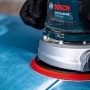 Bosch Exzenterschleifer mit Schleifblatt C470 K60 beim Schleifen einer blauen Oberfläche.