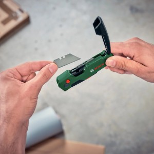 Bosch Klappmesser: Hand legt Klinge in grünes Cuttermesser mit Klingenfach.