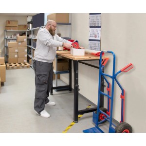 Mann verpackt Ware auf höhenverstellbarer rikta Werkbank mit Holzplatte und schwarzem Gestell.