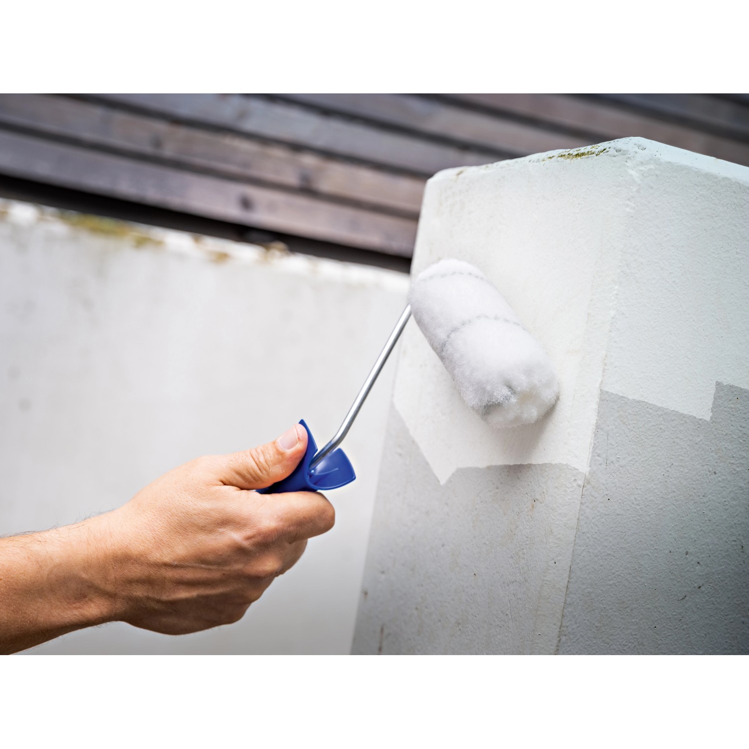 Hand streicht Betonpfeiler mit grauer Lackierwalze LUX PRO (10 cm).