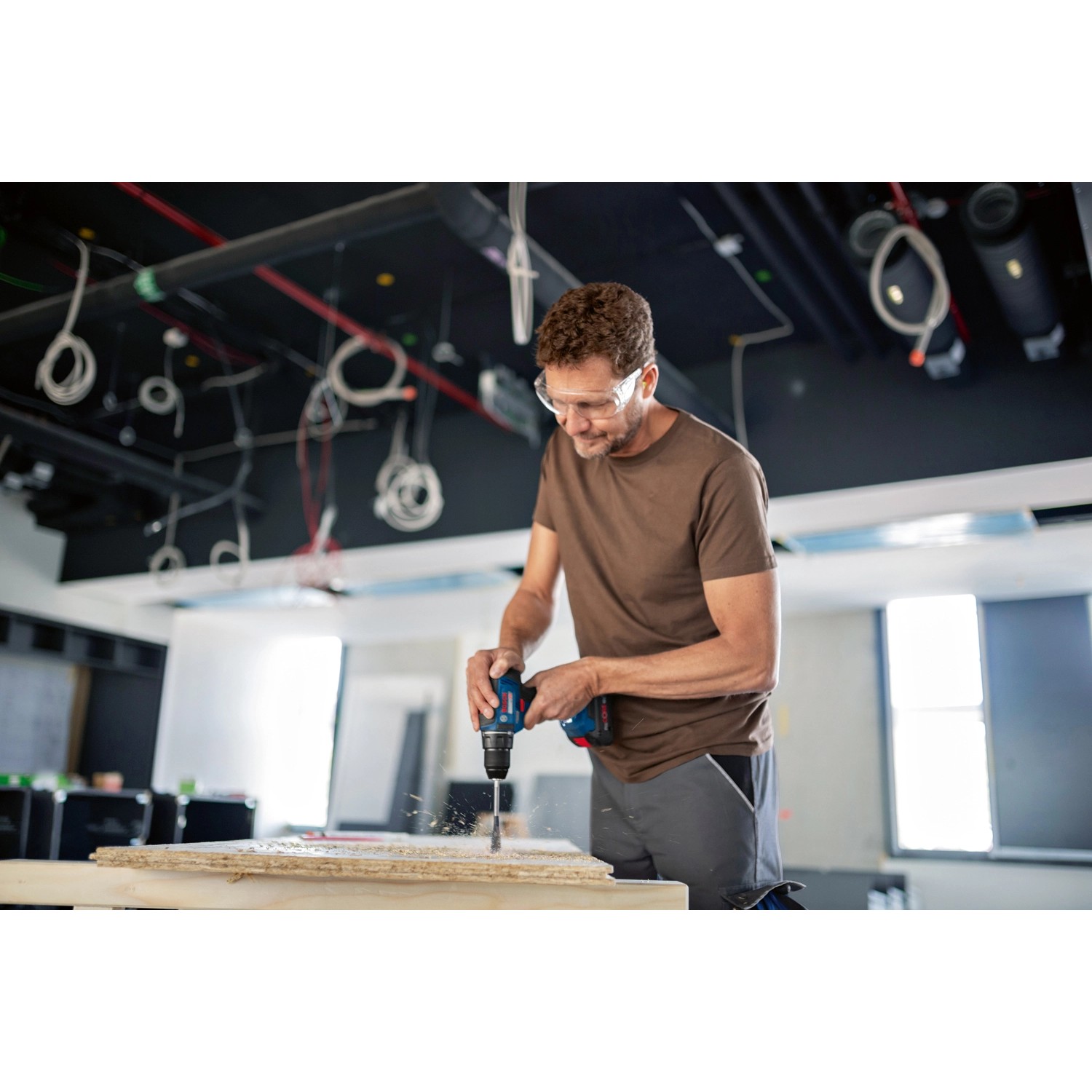Mann bohrt mit Bosch Professional Akku-Bohrschrauber GSR 18V-55 ein Loch in Holz.