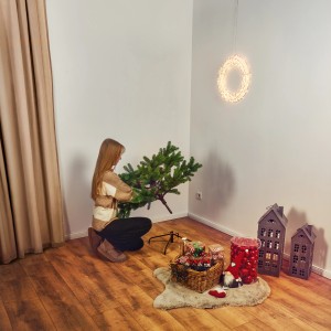 Frau setzt grüne Kunsttanne Fundy (150 cm) zusammen. Weihnachtsbaum mit Ständer im Innenraum.