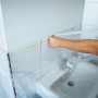 Person klebt Wand über Waschbecken mit LUX-TOOLS 2-in-1 Krepp und Folie ab, schützt vor Farbspritzern.