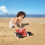 Kind spielt mit rotem Hape Dünen-Buggy Sandspielzeug am Strand.