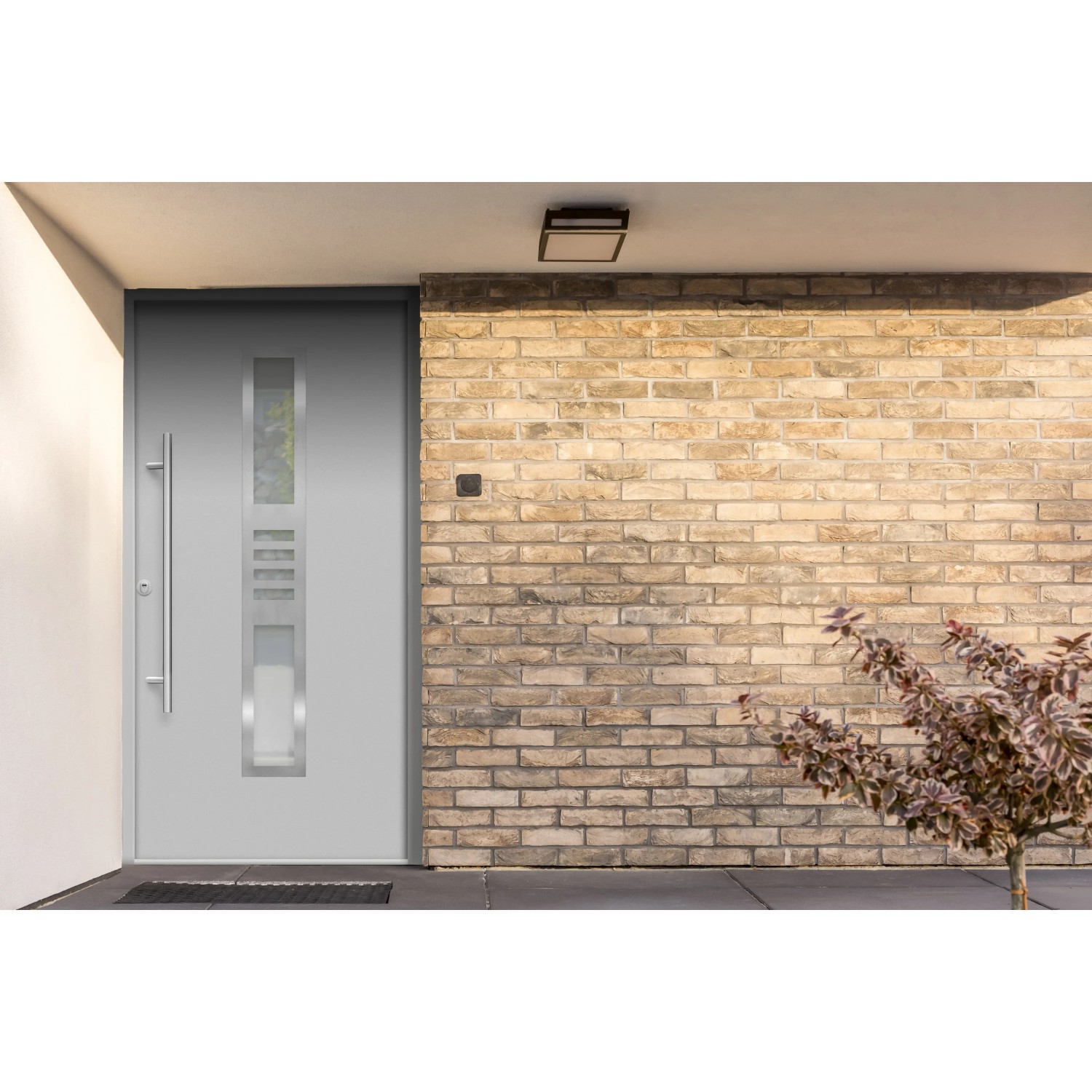 Graue Sicherheits-Haustür ThermoSpace Köln Prime RC2 mit Edelstahlgriff und Glaseinsatz vor Backsteinwand.