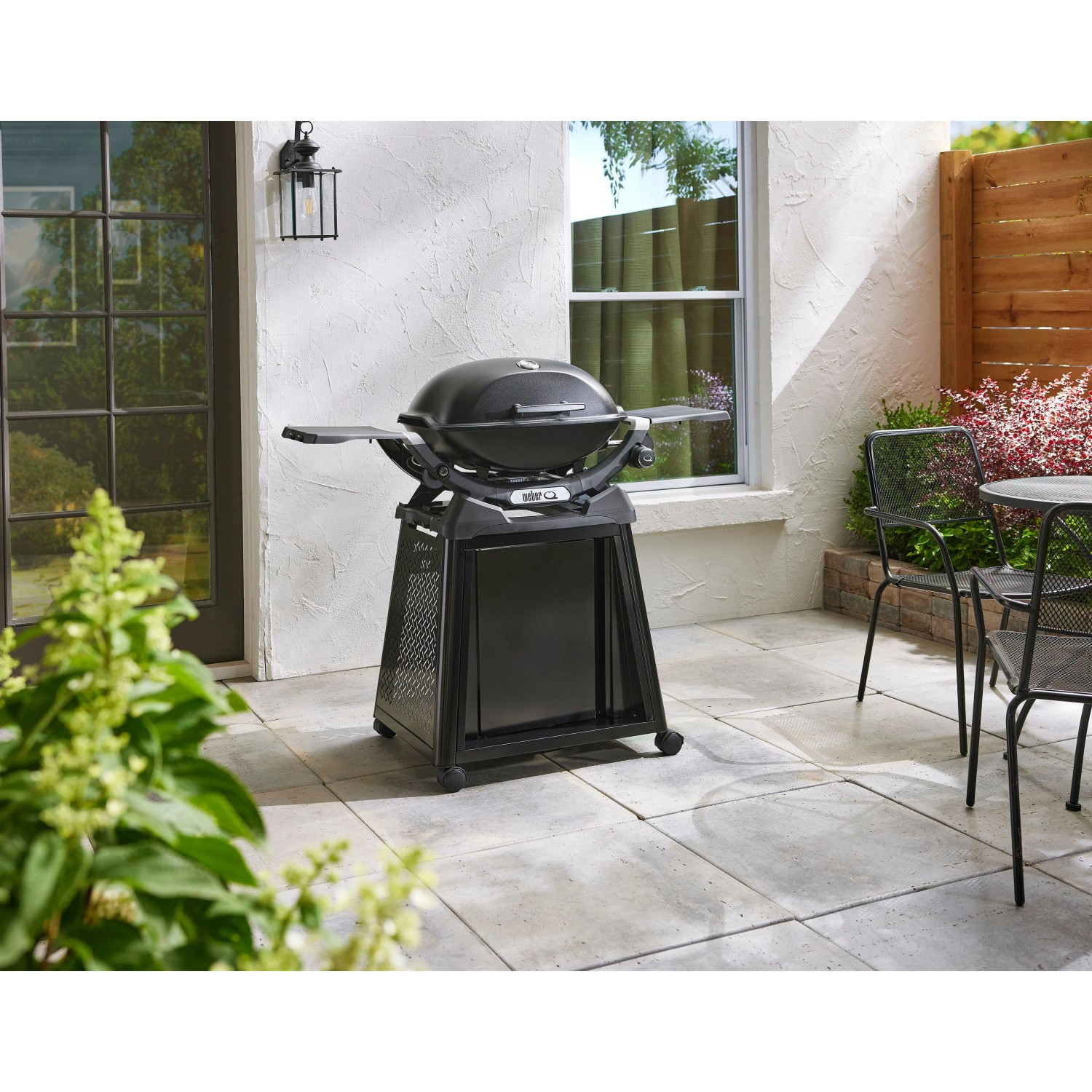 Schwarzer Weber Gasgrill Q2200N mit Stand und Seitentischen auf einer Terrasse.