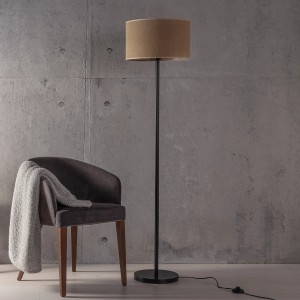 Schwarze Brilliant Stehleuchte Aniela mit Natur-farbenem Textilschirm neben einem Sessel.